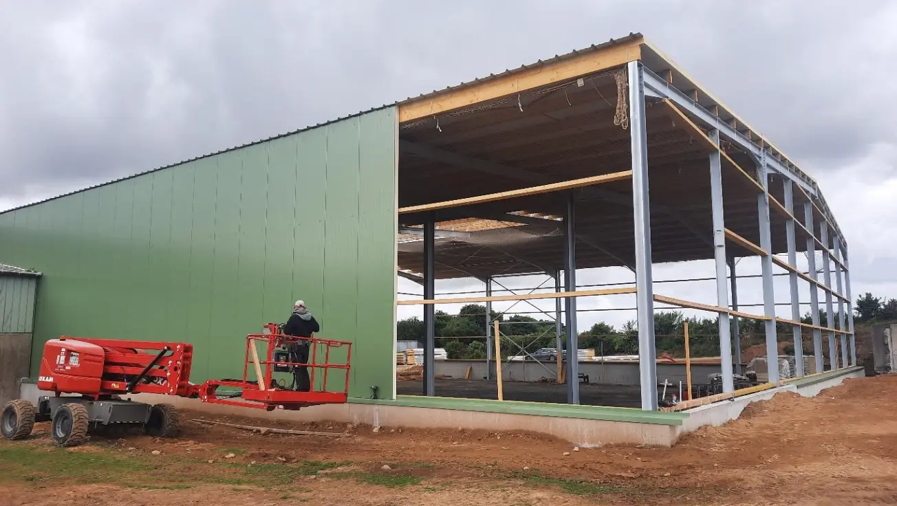 Bardage en panneaux sandwichs vert et charpente métallique du hangar de stockage réfrigéré de Landivisiau, avec une nacelle au pied du bâtiment