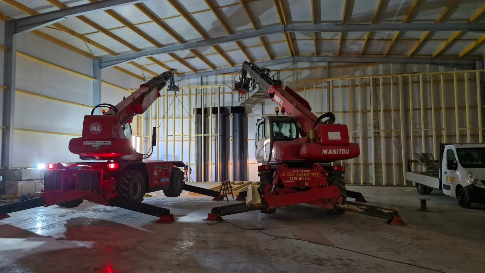 Intérieur d'un bâtiment réfrigéré en charpente métallique et pannes bois, avec deux télescopiques devant l'ossature en bois du caisson de réfrigération